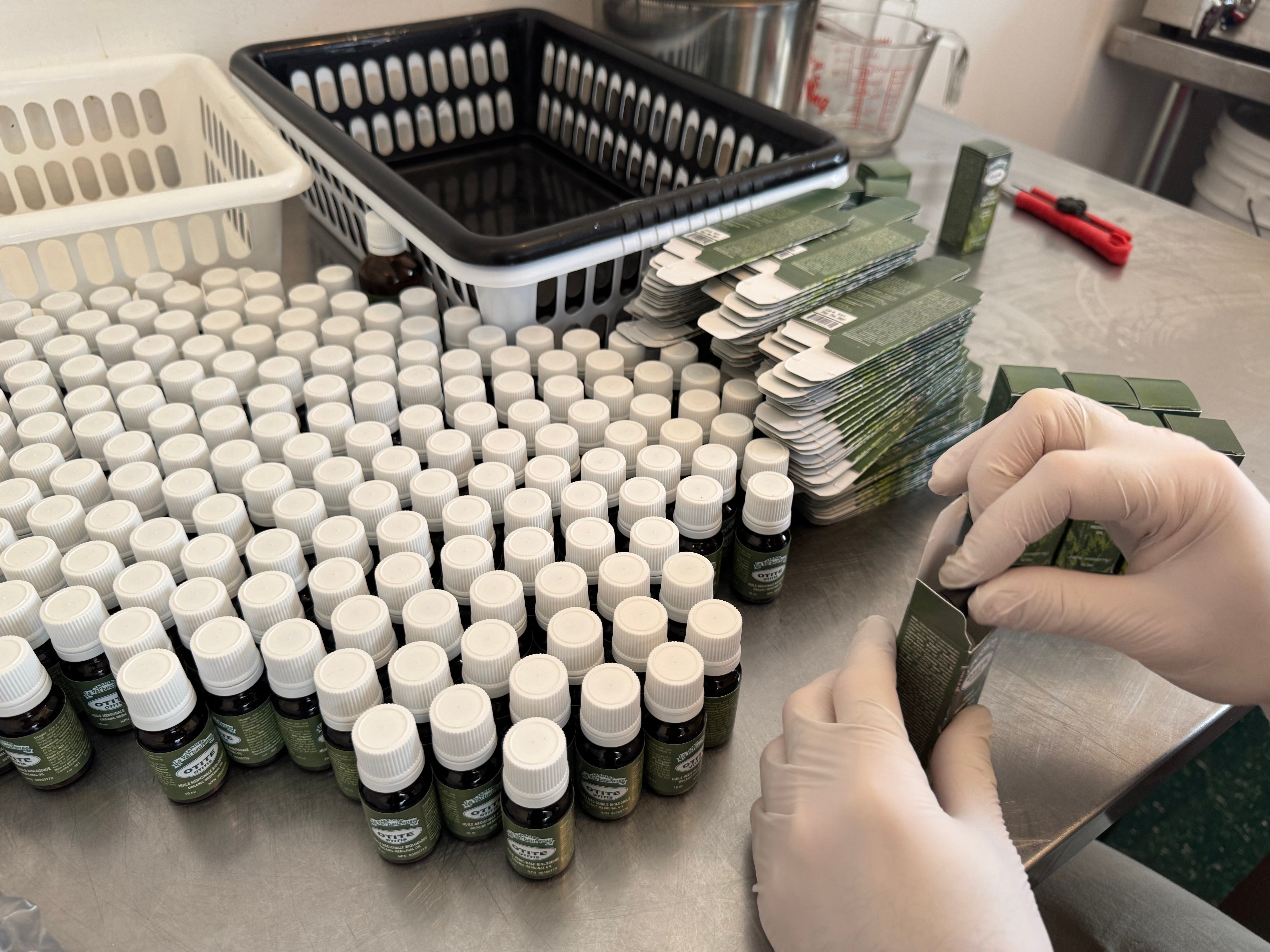 Opération d'emballage de l'Huile Otite de La Val'Heureuse. Dans le laboratoire, de nombreuses petites bouteilles sont emballées une à une dans un carton individuel.